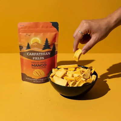 Hand reaching into a black bowl of freeze-dried mango slices next to pouch